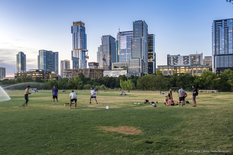 City view of Austin's downtown skyline. People are lounging in the grass playing games.